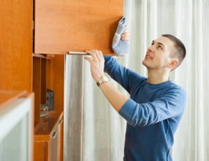 Smiling man cleaning wooden furniture with rag at home